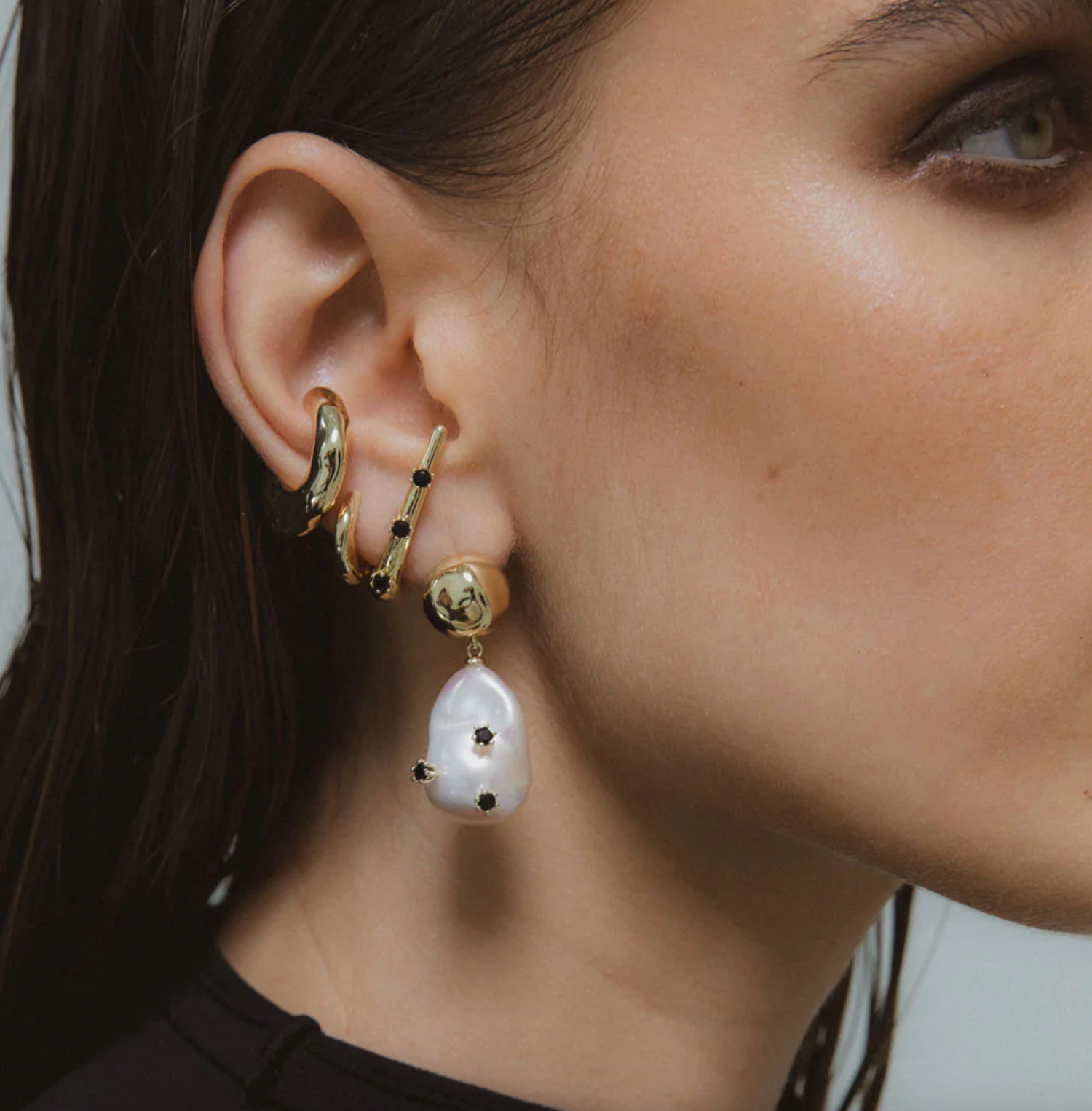 Close-up of a woman's ear wearing gold hoop earrings with black stones and a pearl earring.