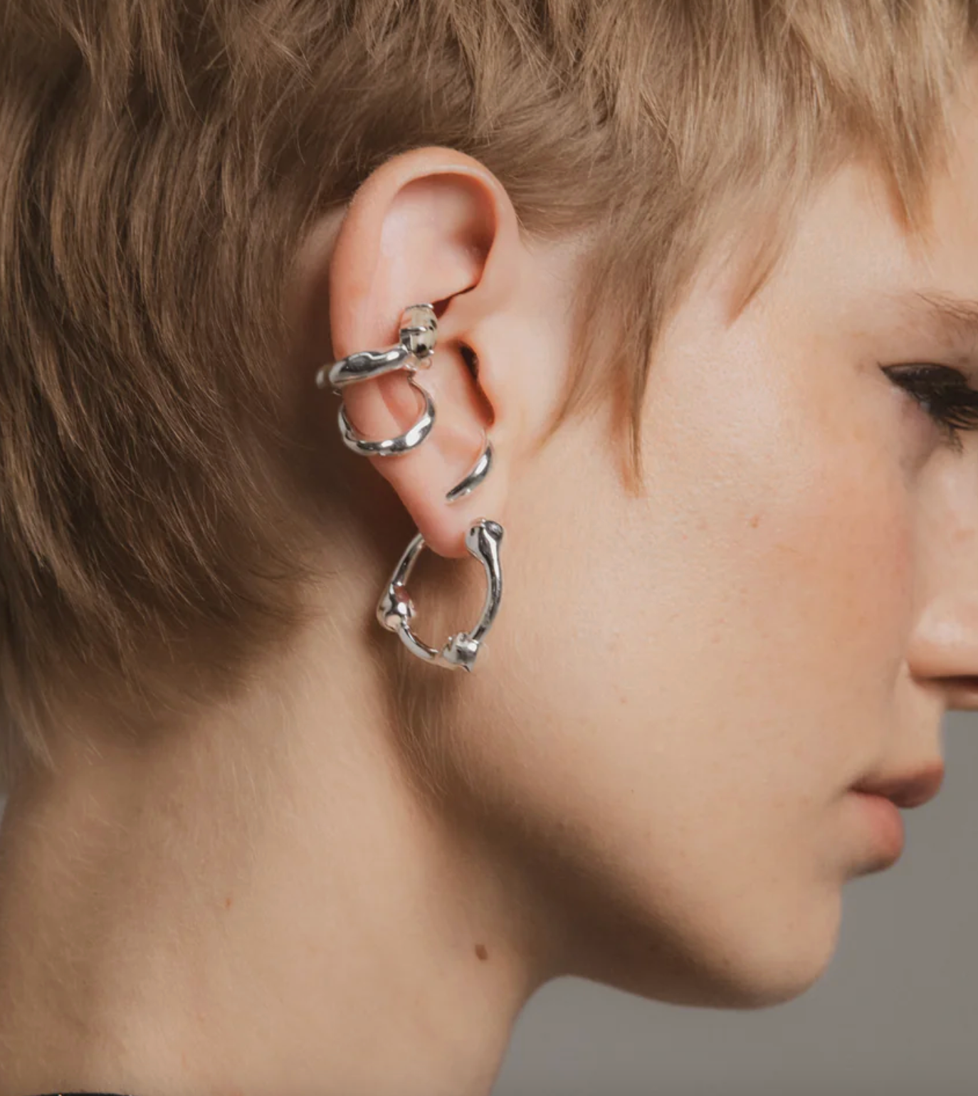Close-up of a person wearing silver hoop earrings with a neutral background