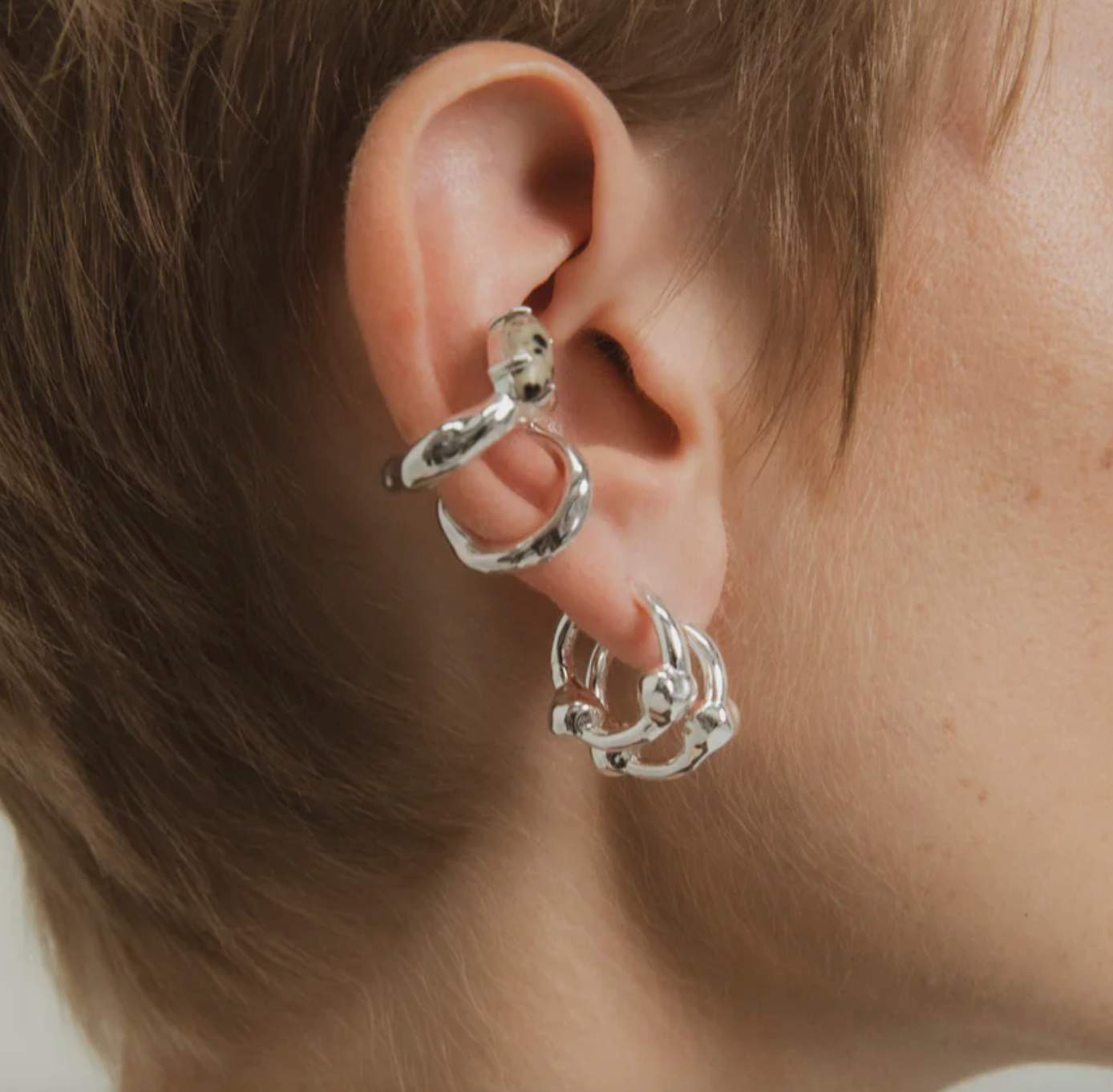 Close-up of an ear wearing silver hoop earrings with a blurred background