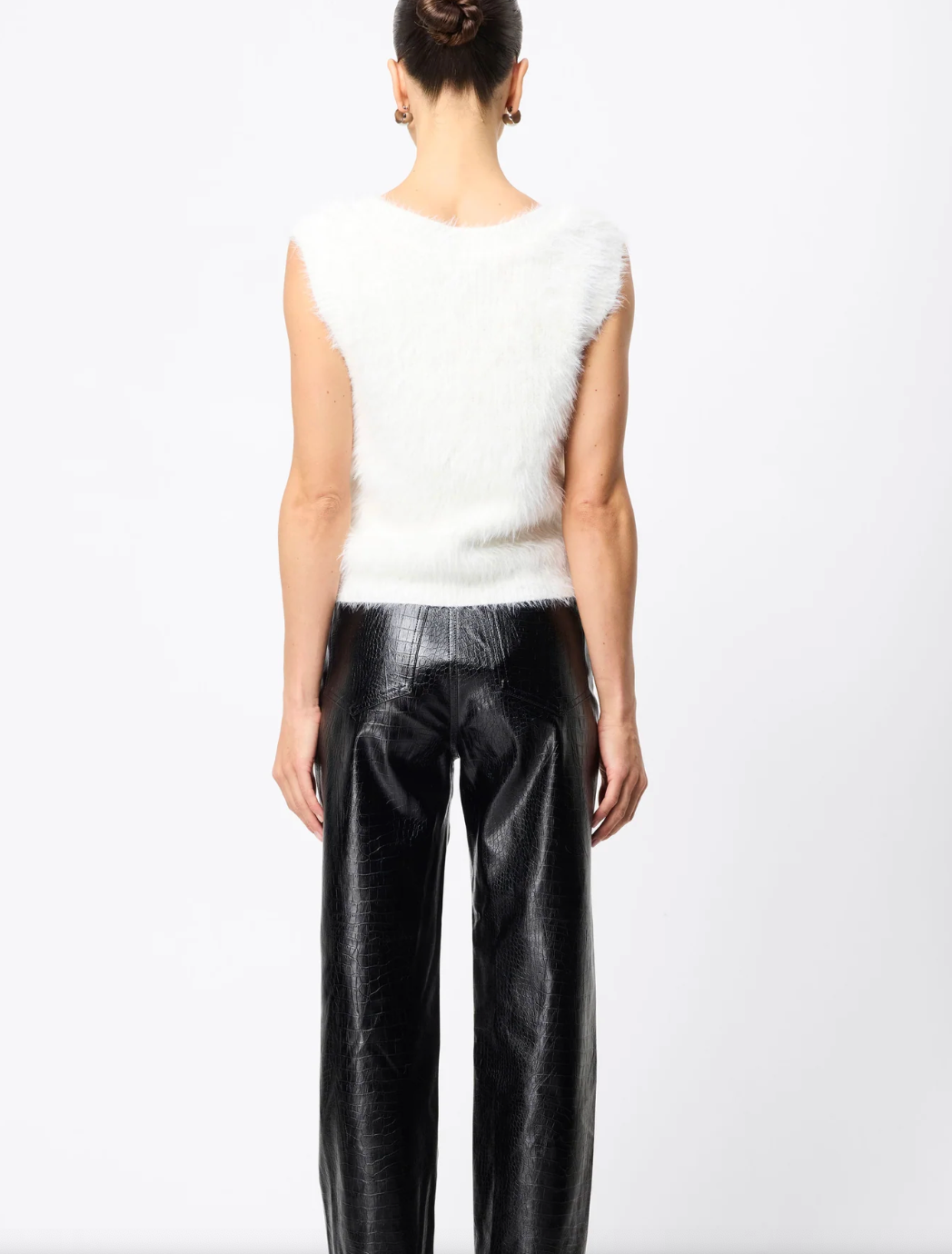 Person wearing a white sleeveless top and black pants on a white background