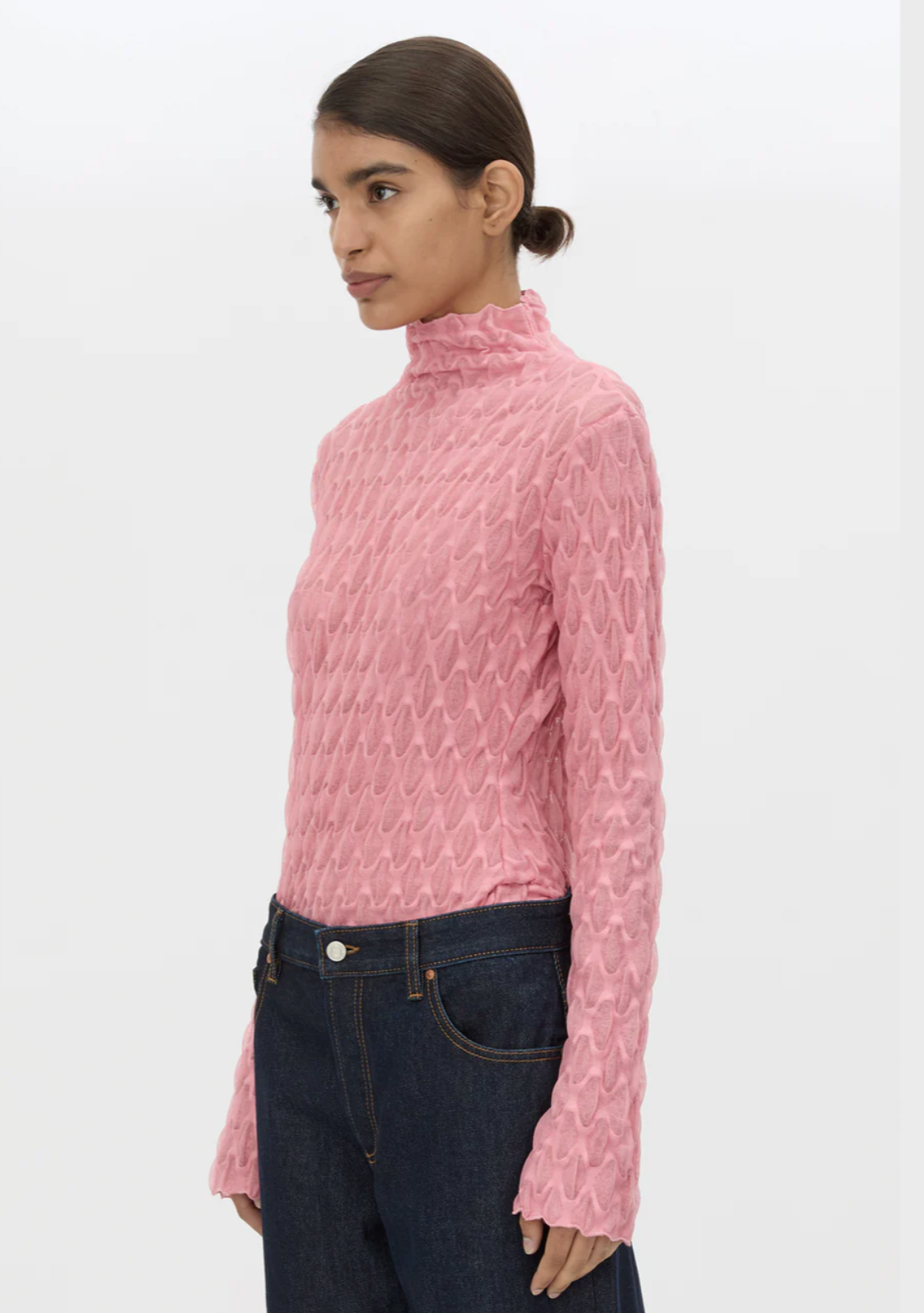 Woman wearing a pink textured sweater and dark jeans on a white background
