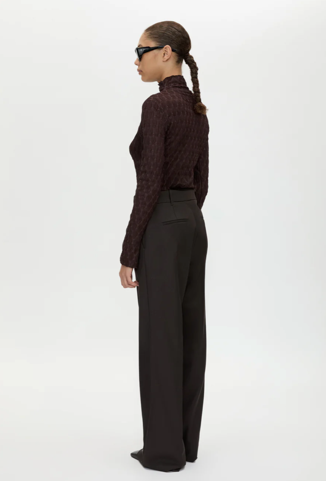 Person wearing a brown turtleneck sweater and black pants on a white background