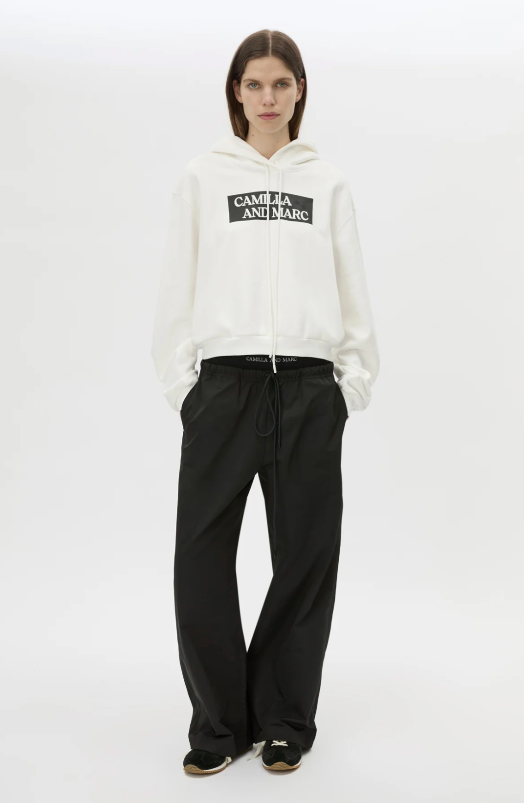 Person wearing a white hoodie with a logo and black pants on a white background