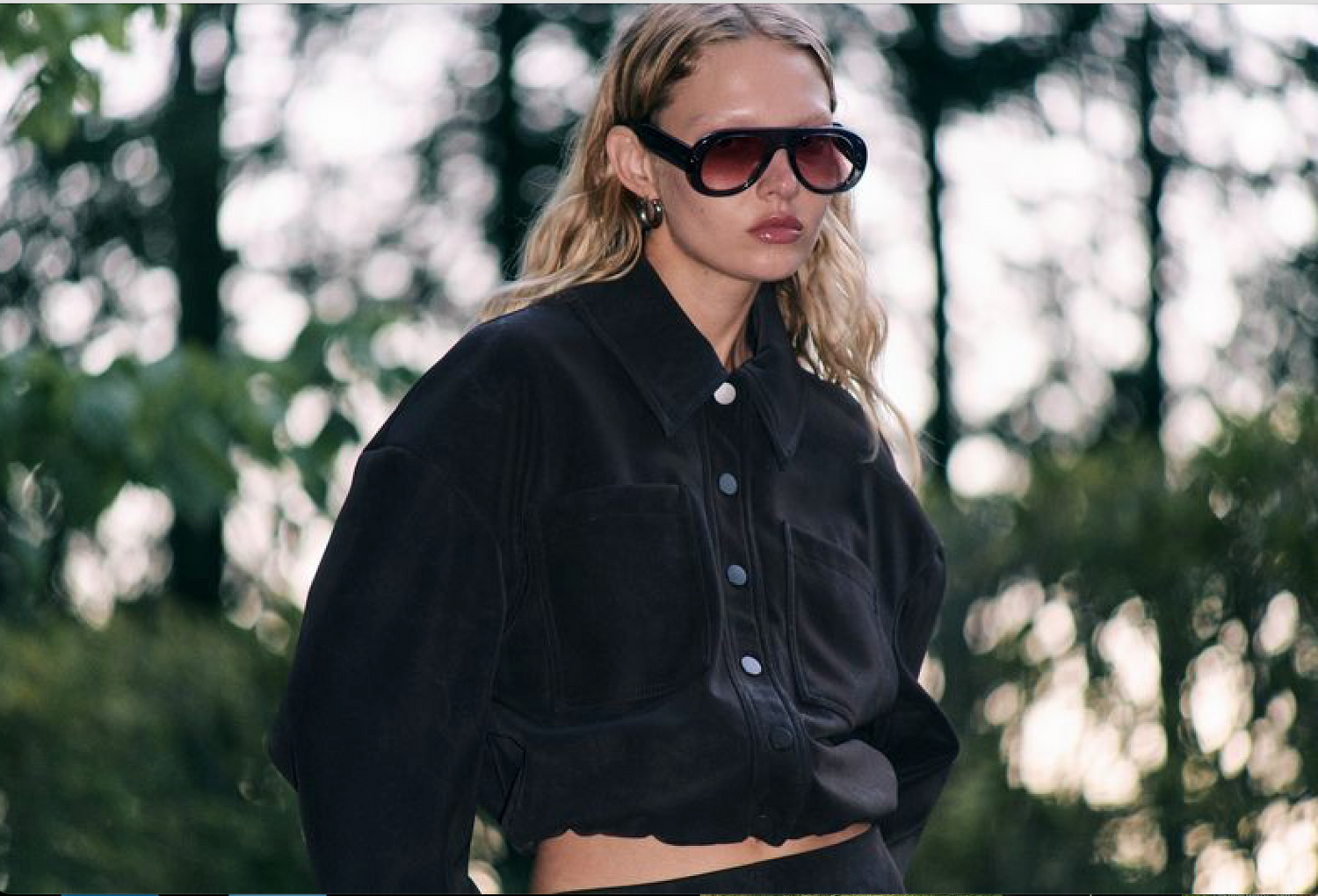 Person wearing a black jacket and sunglasses with a blurred natural background