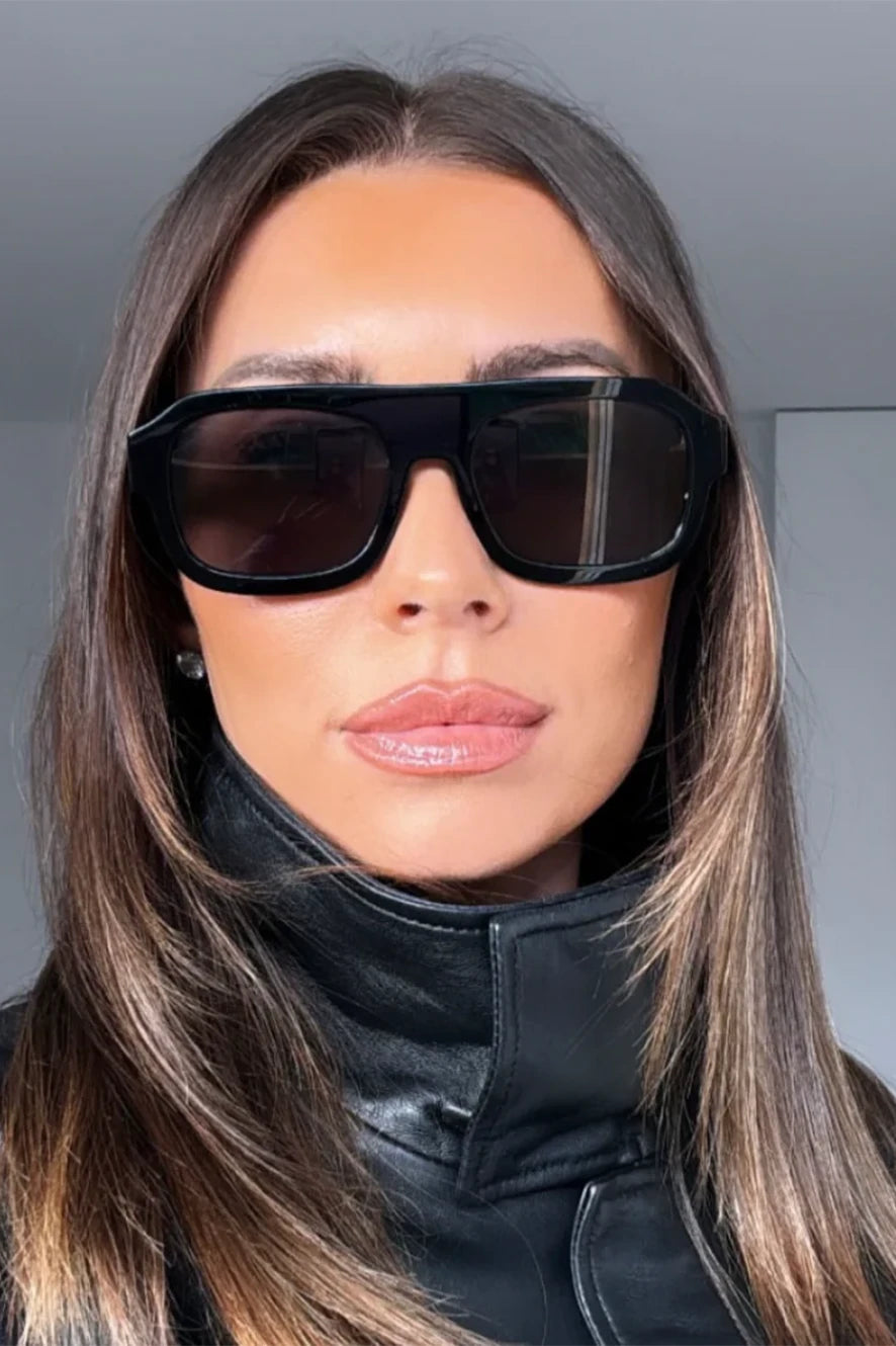 Woman wearing black sunglasses and a black outfit indoors.