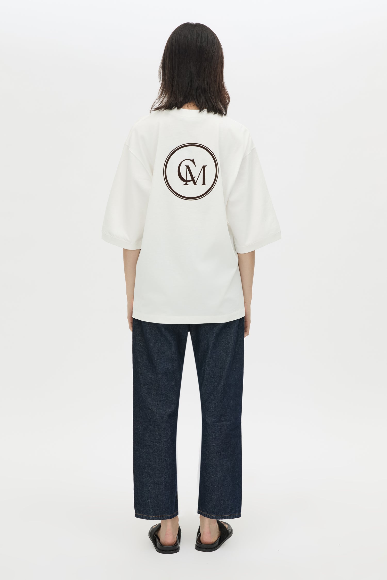 Person wearing a white shirt with a logo on the back against a white background