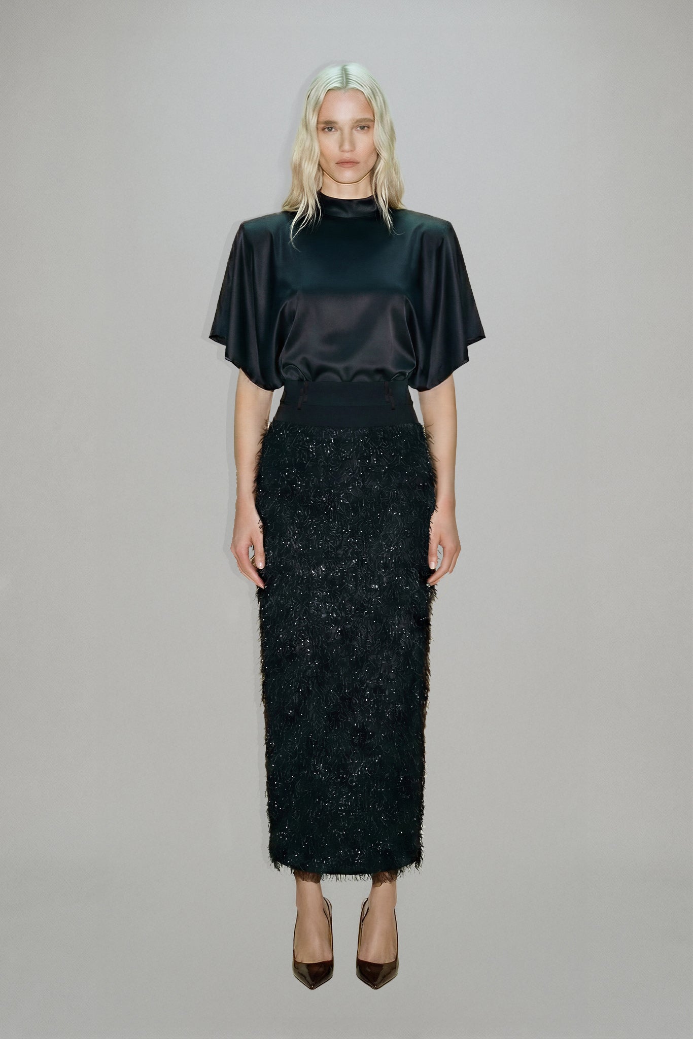 Woman wearing a black outfit with a textured skirt on a plain background