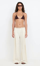 Woman wearing a brown bikini top and cream pants on a white background