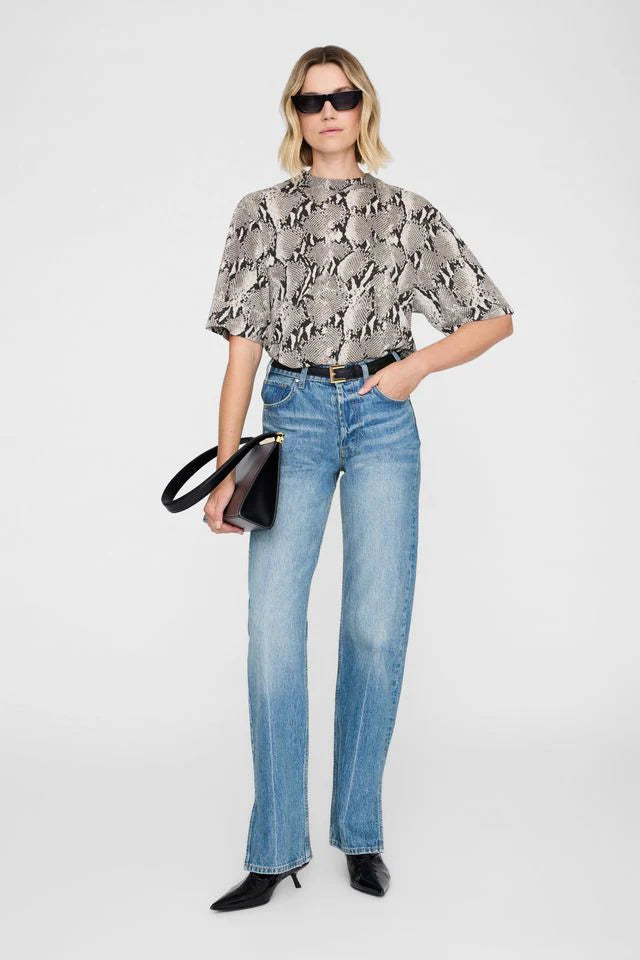 Woman wearing a python tee shirt, blue jeans, and black shoes on a white background