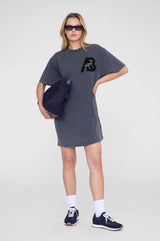 Woman wearing a gray t-shirt dress with a logo, holding a blue bag on a white background