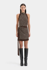Model wearing a patterned dress with a belt and black boots on a white background