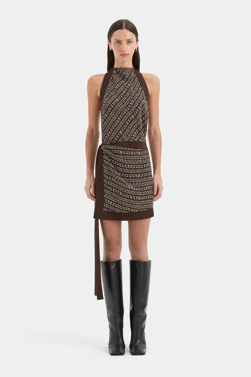 Model wearing a patterned dress with a belt and black boots on a white background