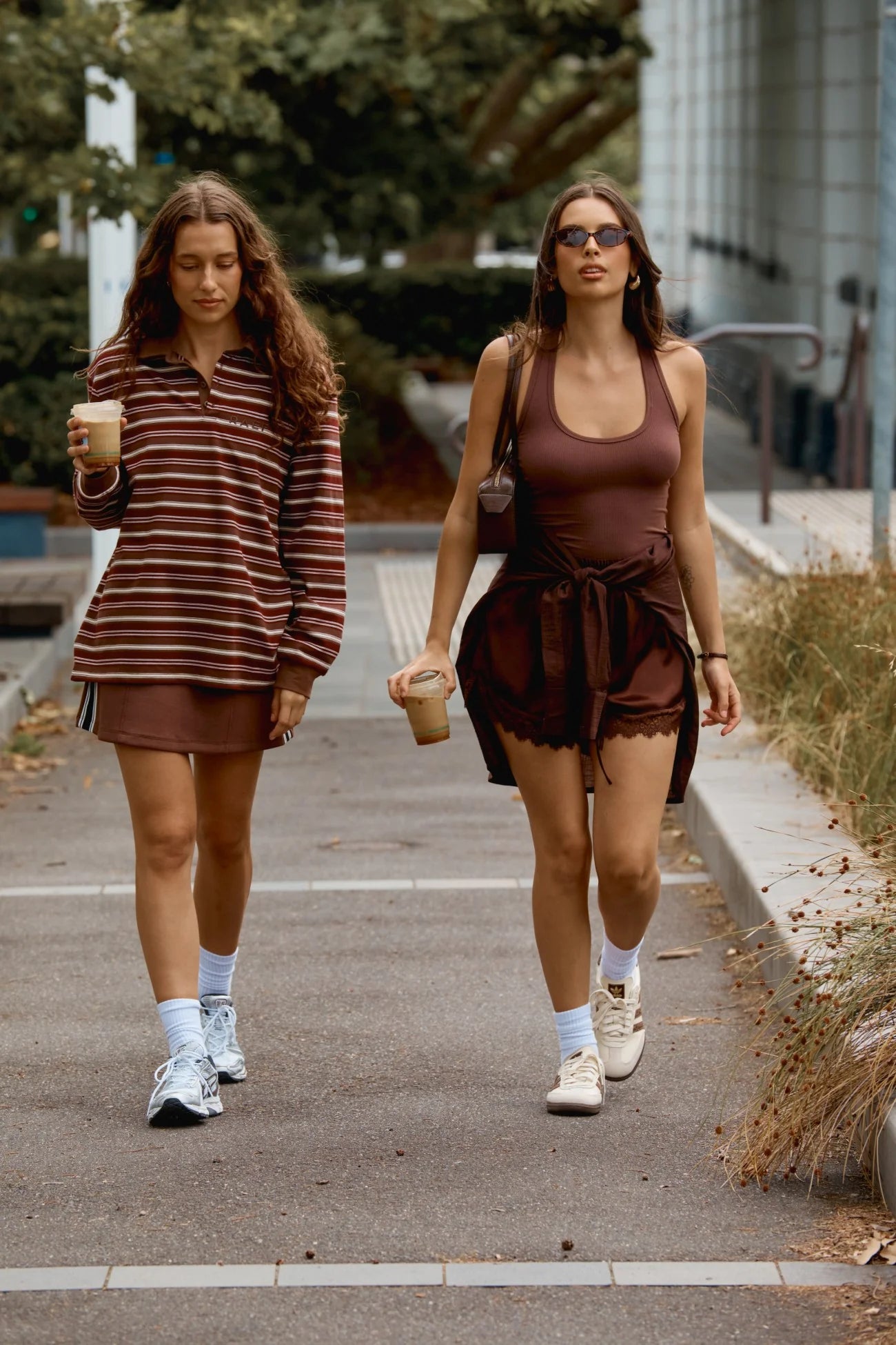 Two women walking on a sidewalk, both wearing brown outfits.