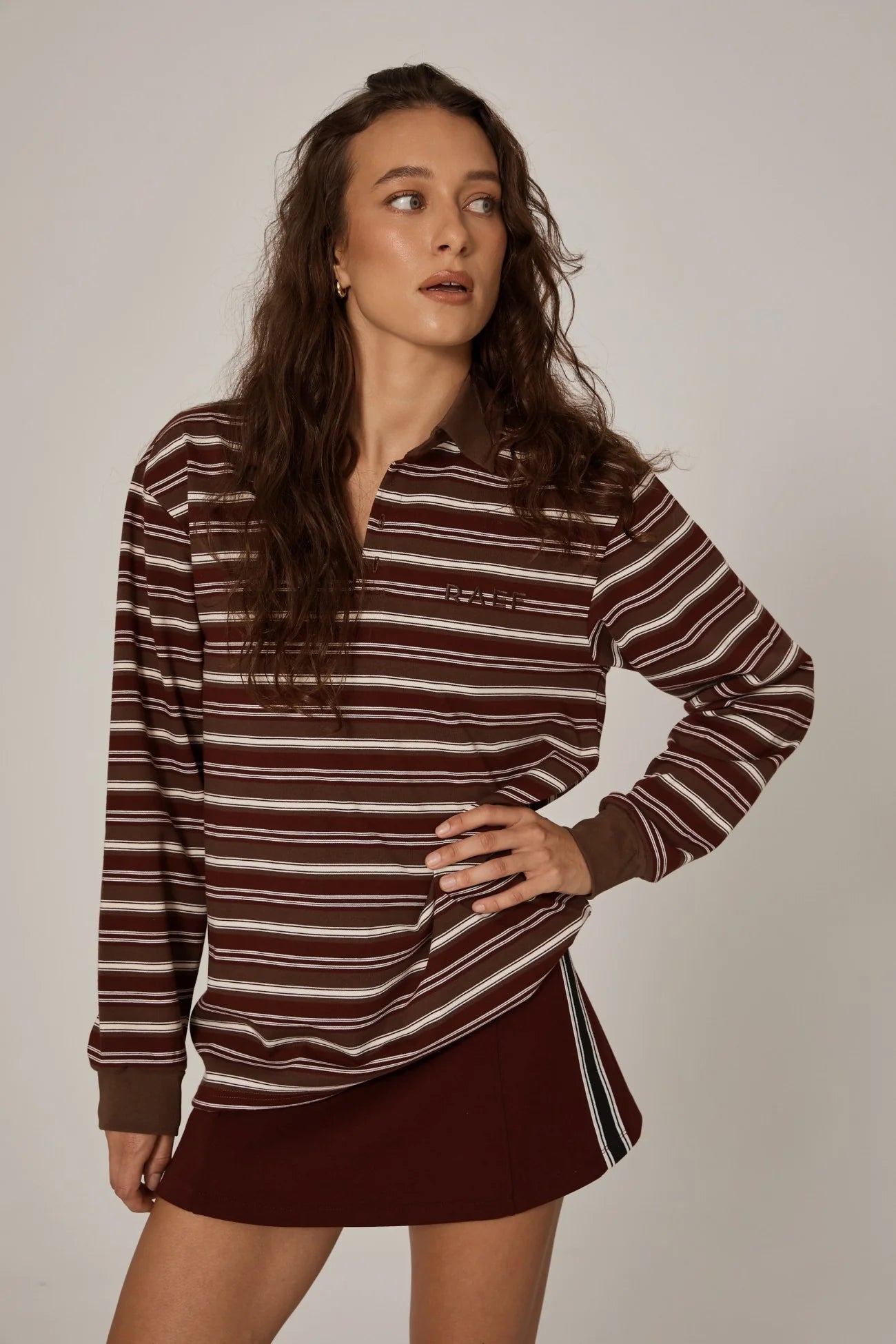 Woman wearing a brown and white striped shirt with a maroon skirt on a plain background