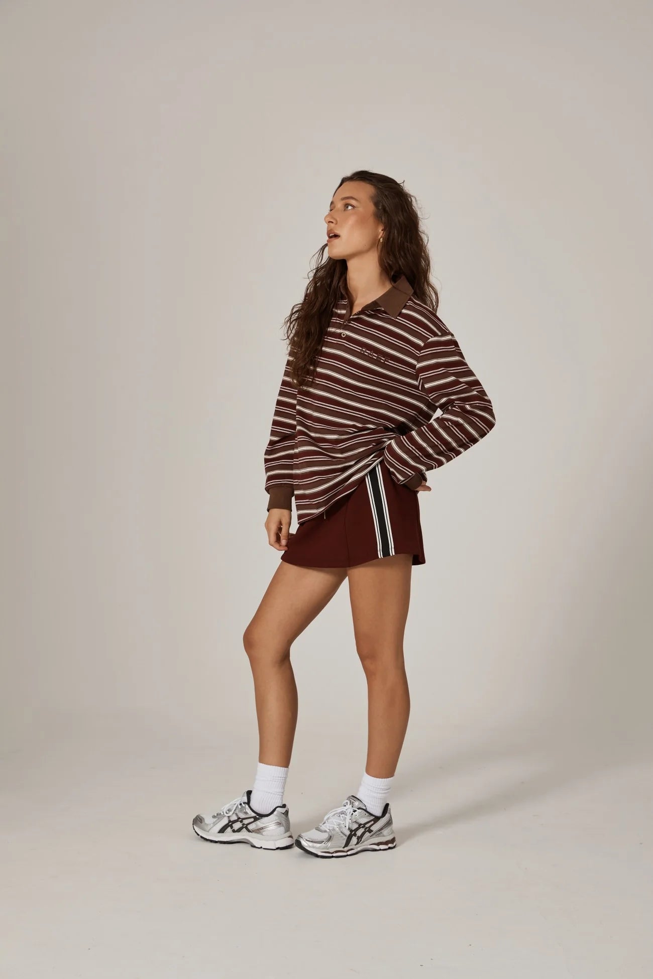 Woman wearing a striped sweater and skirt with white sneakers on a plain background