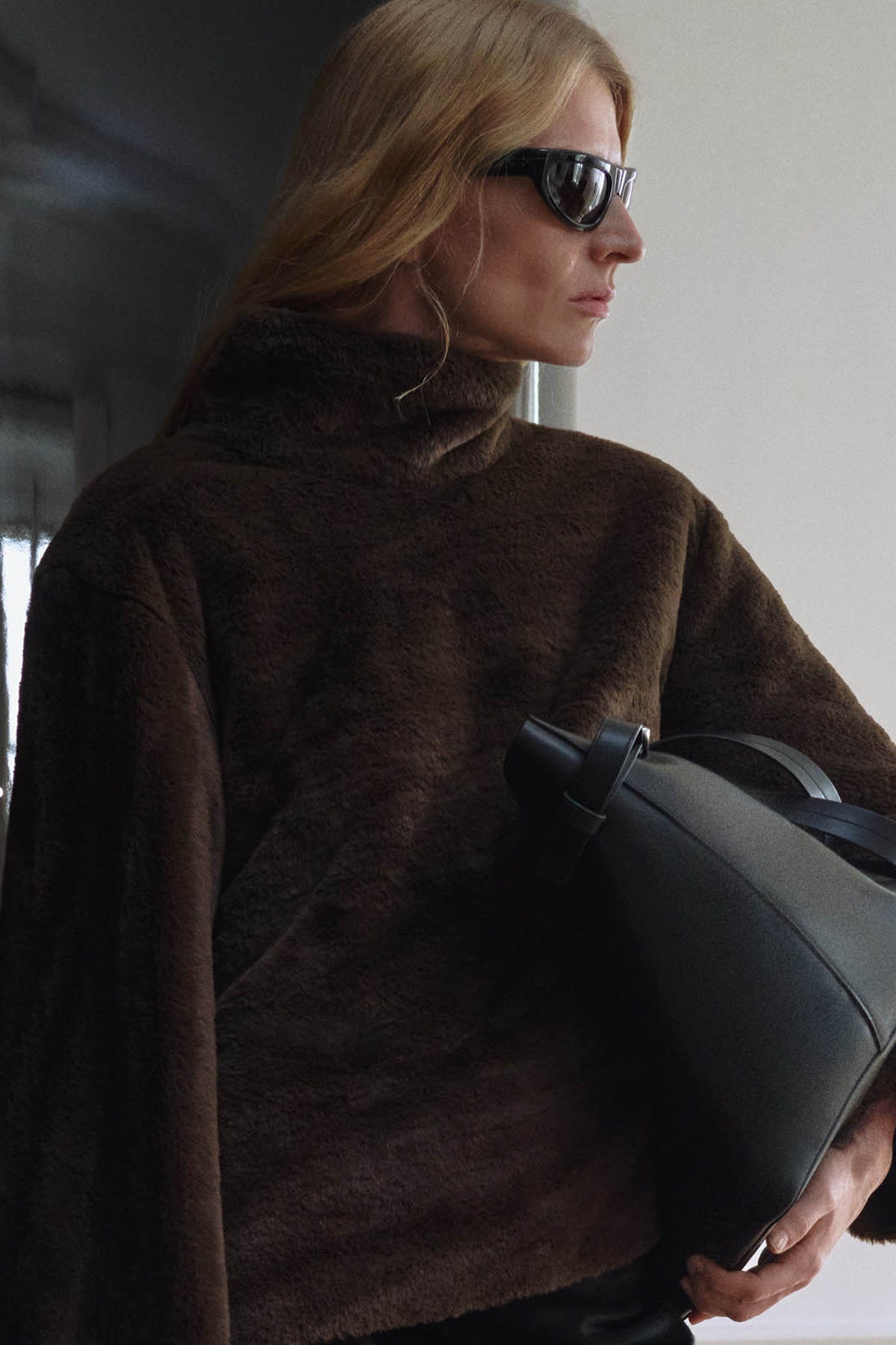 Woman holding a black bag indoors with neutral background