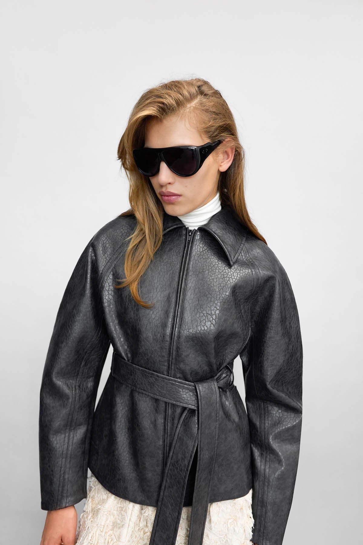 Woman wearing a metallic silver jacket and sunglasses on a white background
