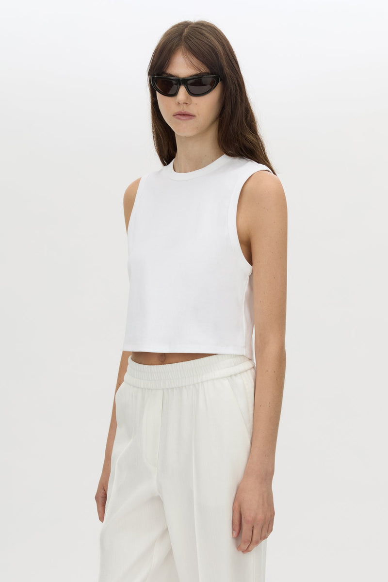 Woman wearing a white sleeveless top and white pants on a plain background