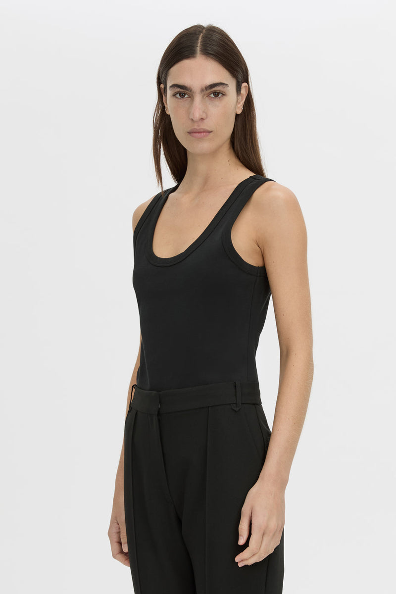 A woman modeling a black sleeveless scoop-neck top with matching black trousers, photographed against a light gray studio background.