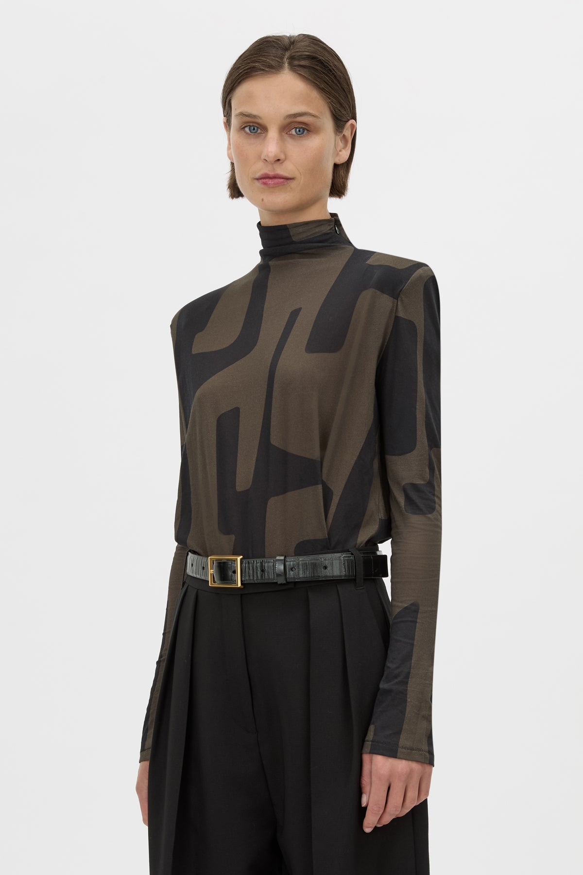 Woman wearing a brown and black patterned blouse with a belt on a white background