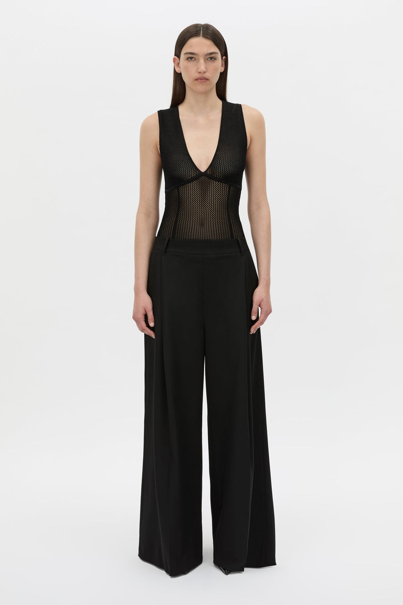 A model wearing a black sleeveless wide-leg jumpsuit with a sheer mesh corset-style bodice, photographed against a plain light gray studio background.