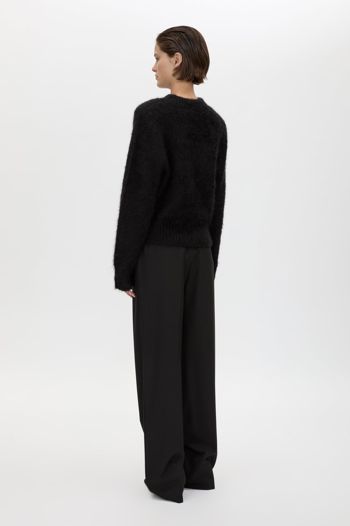 Person wearing a black sweater and wide-leg pants on a white background