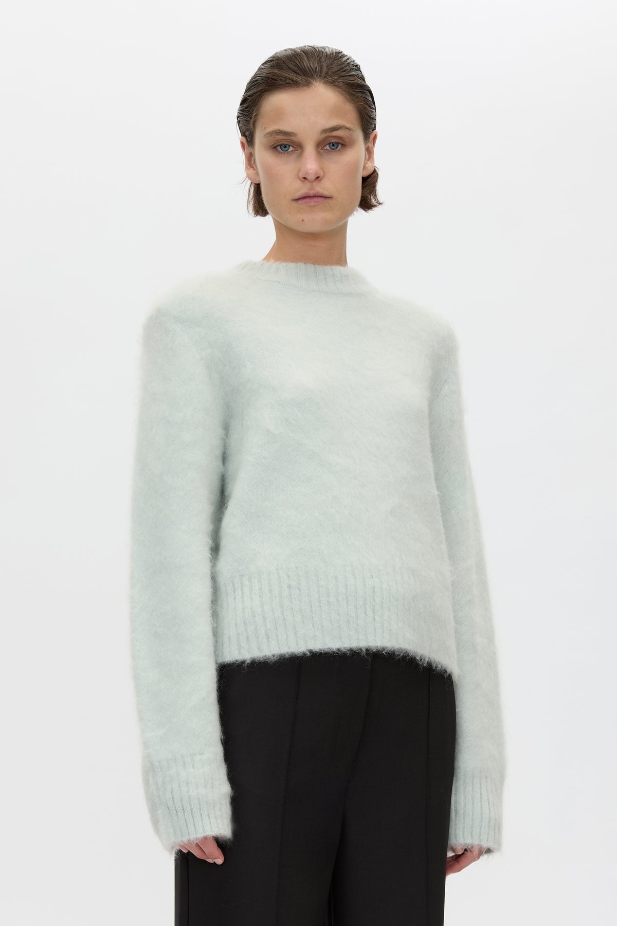 Person wearing a light green sweater and black pants on a white background
