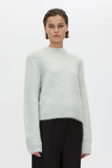 Person wearing a light green sweater and black pants on a white background