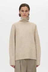 Person wearing a beige turtleneck sweater and pants on a white background
