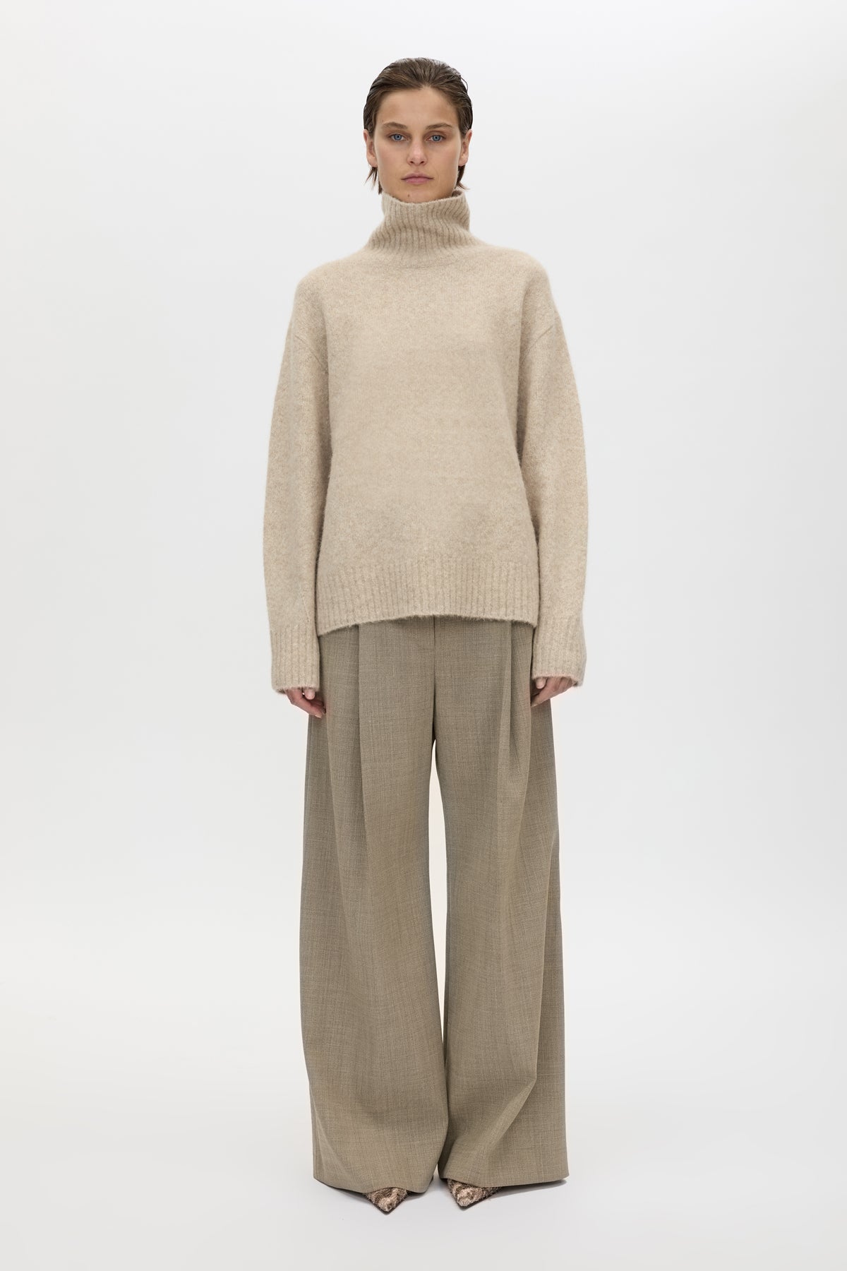 Person wearing a beige turtleneck sweater and wide-leg pants on a white background