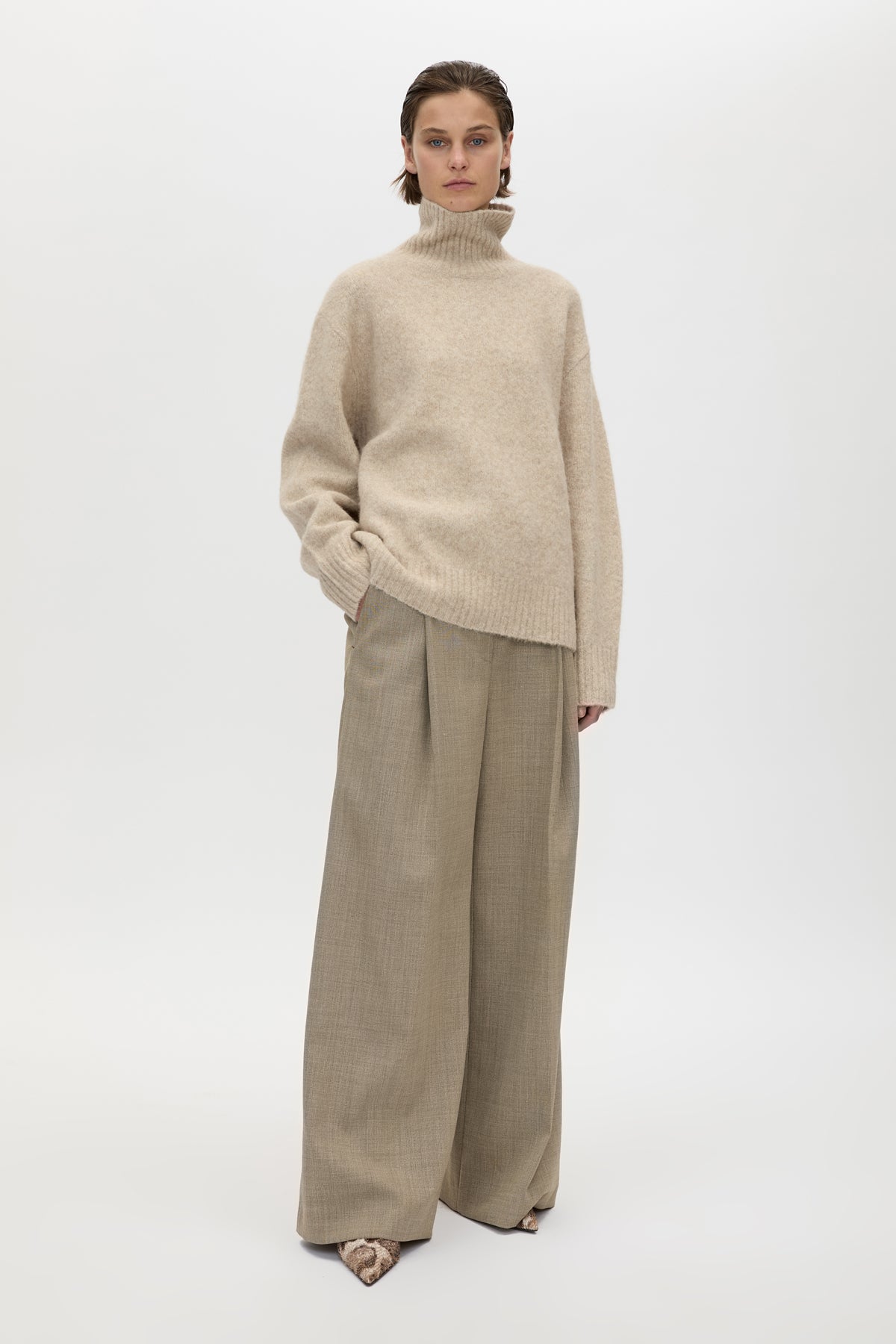 Person wearing a beige turtleneck sweater and wide-leg pants on a white background