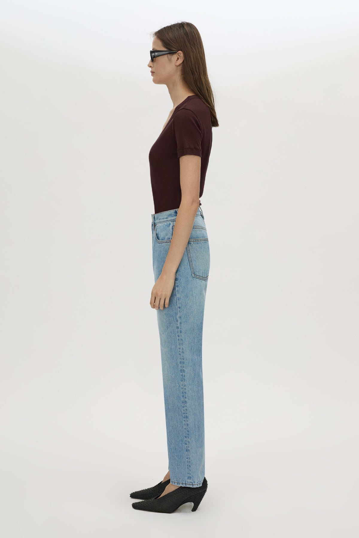 Woman wearing a dark top and light blue jeans on a white background