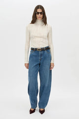 Woman wearing a cream turtleneck, blue jeans, and sunglasses on a white background