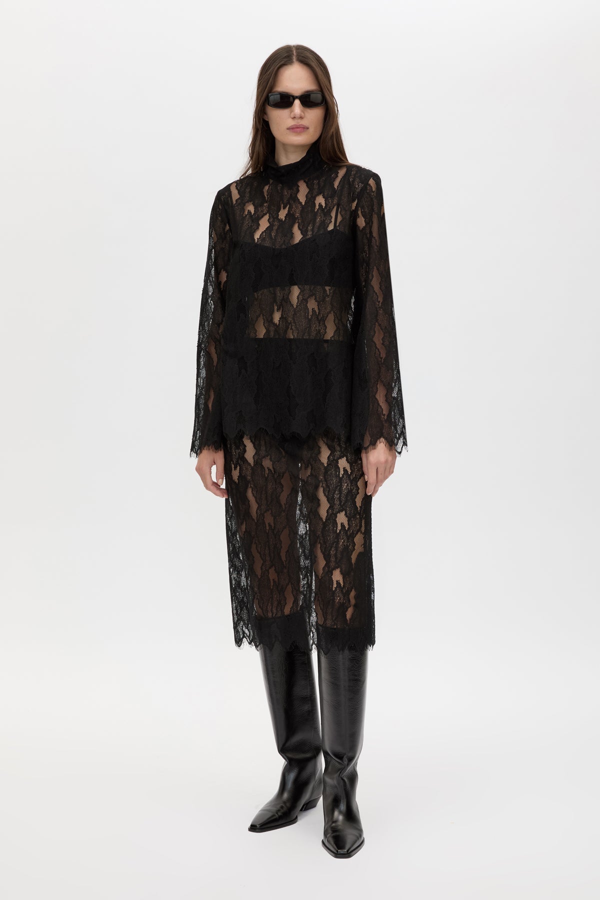 Model wearing a black lace dress with long sleeves and black boots on a white background