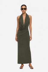 A woman modeling a sleeveless olive green halter maxi dress with a draped cowl neckline and gathered ruching at the waist, photographed against a plain light gray studio background.