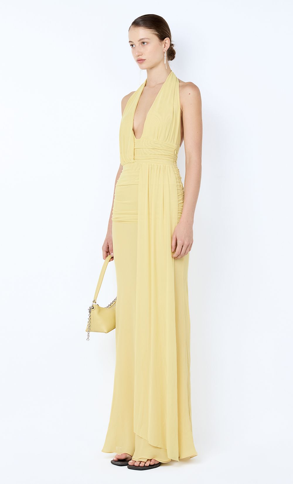 Woman wearing a yellow jumpsuit holding a matching handbag on a white background