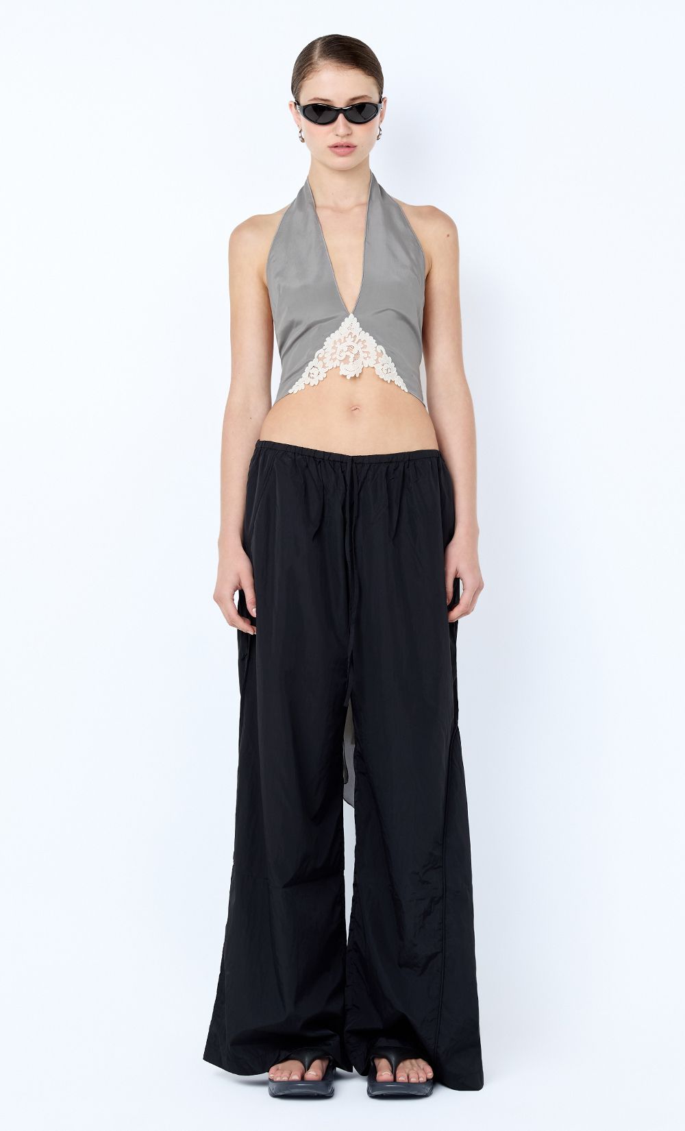 Woman wearing a gray halter top with lace detail and black wide-leg pants on a white background