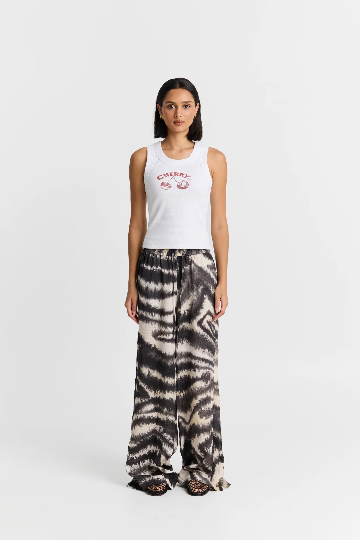 Woman wearing a white tank top with text and tie-dye pants on a white background