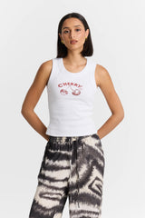 Woman wearing a white tank top with 'CHERRY' print and tie-dye pants on a light gray background