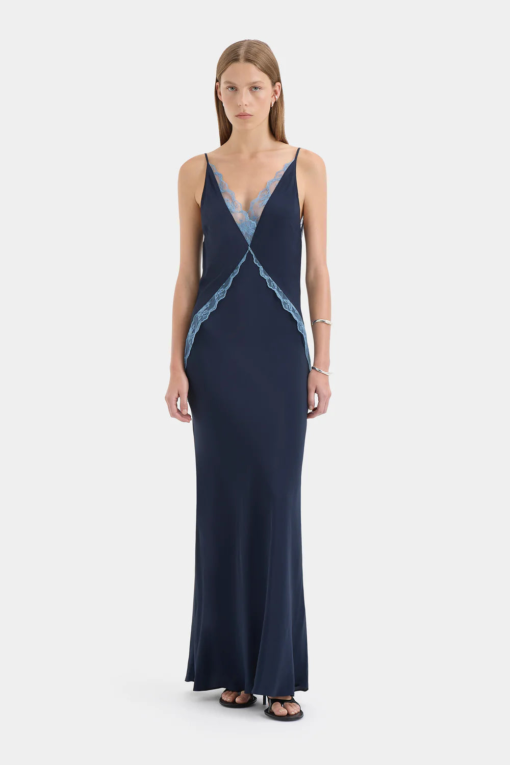 Woman wearing a navy evening gown with lace details on a white background