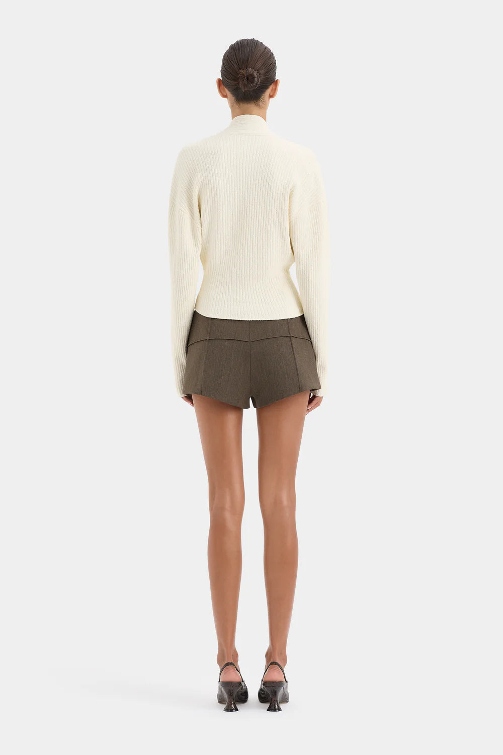 Person wearing a cream sweater and green shorts on a white background