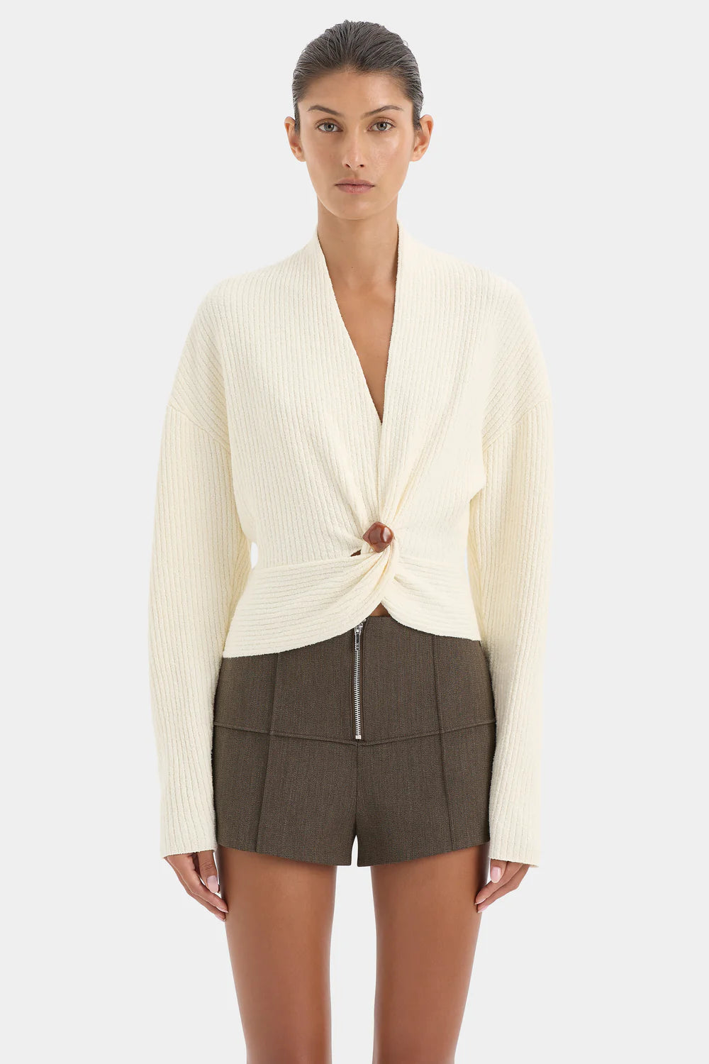 Woman wearing a cream cardigan and brown shorts on a white background