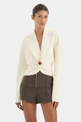 Woman wearing a cream cardigan over a brown top with a white background