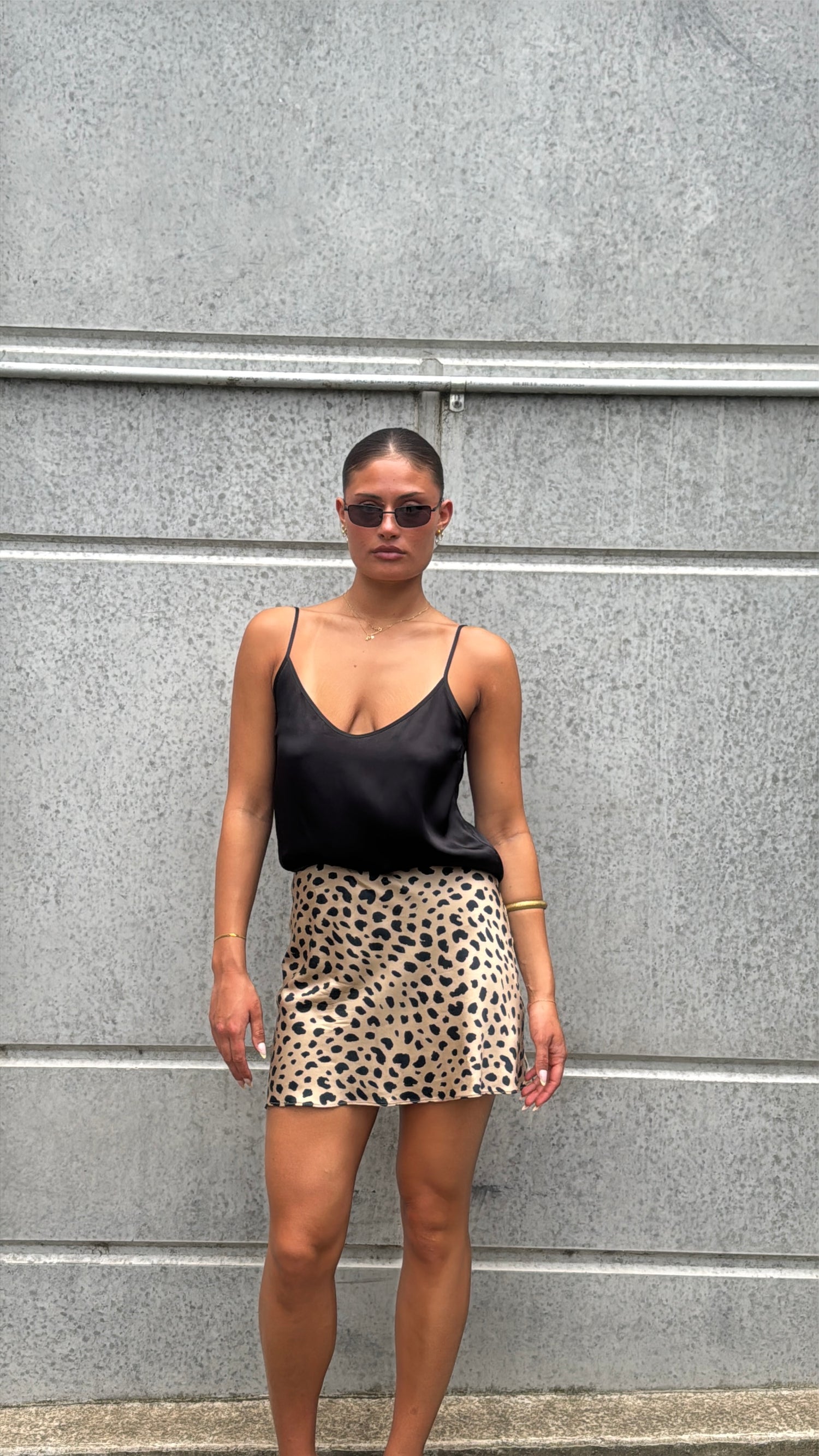 Woman wearing a black top and leopard print skirt against a gray wall.