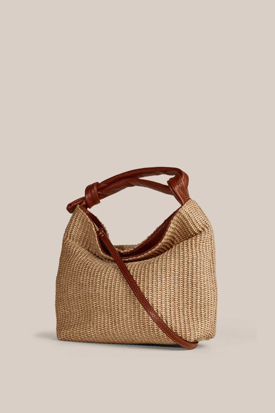 Woven handbag with brown leather handle and strap on a beige background