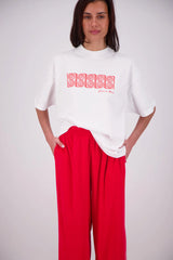 Person wearing a white sweater with red text and red pants on a plain background
