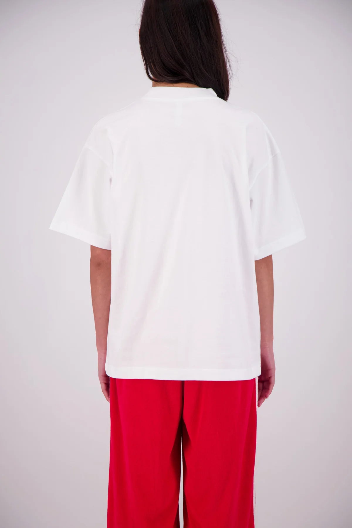 Person wearing a white oversized t-shirt and red pants on a plain background