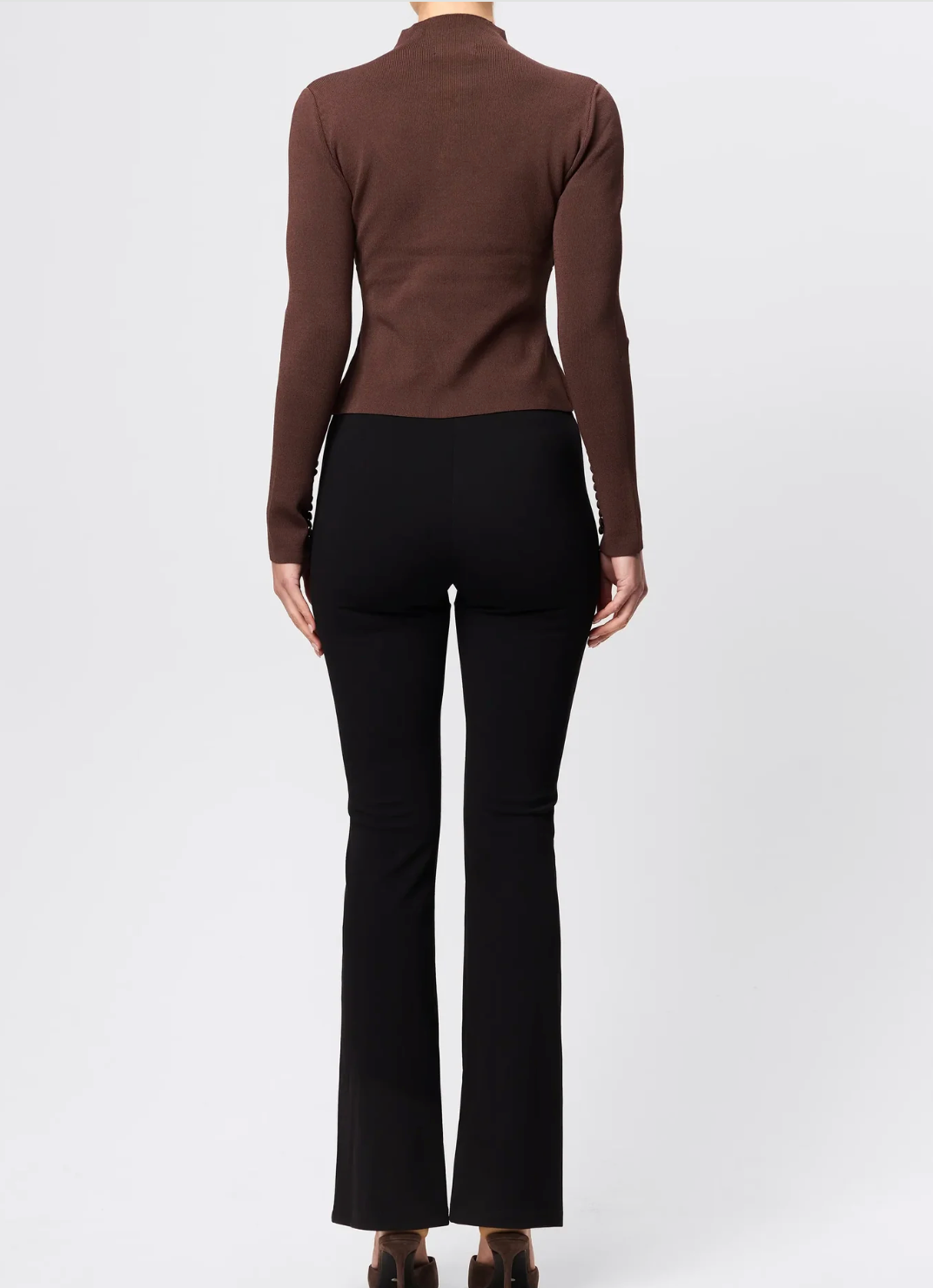 Person wearing a brown turtleneck and black pants on a white background