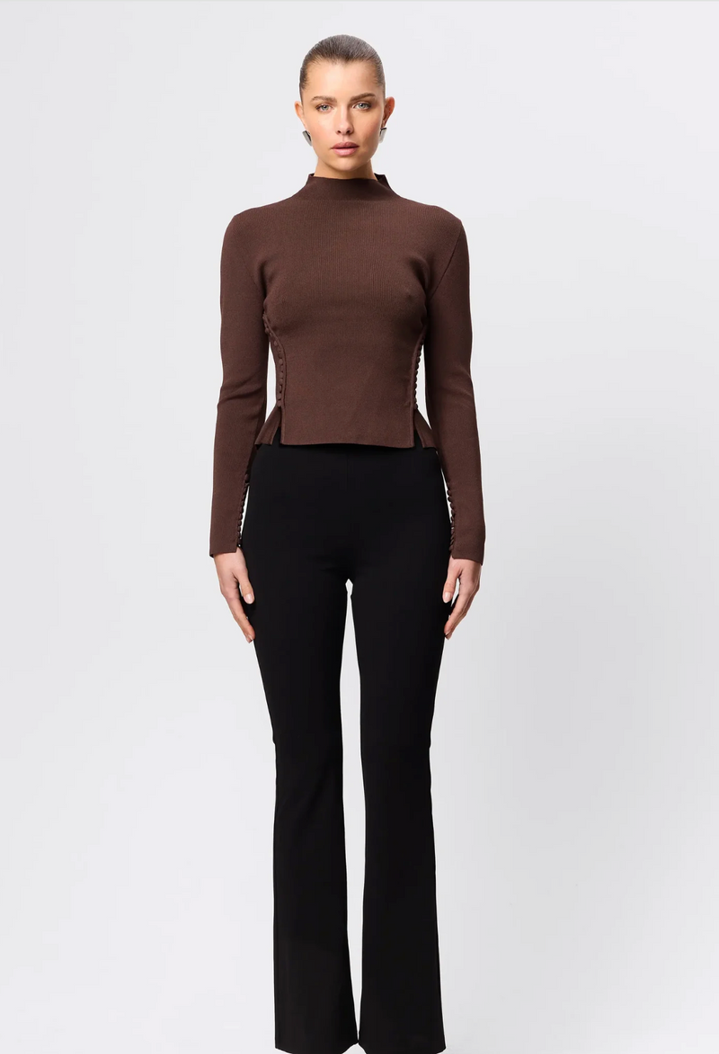 Woman wearing a brown turtleneck top and black pants on a white background