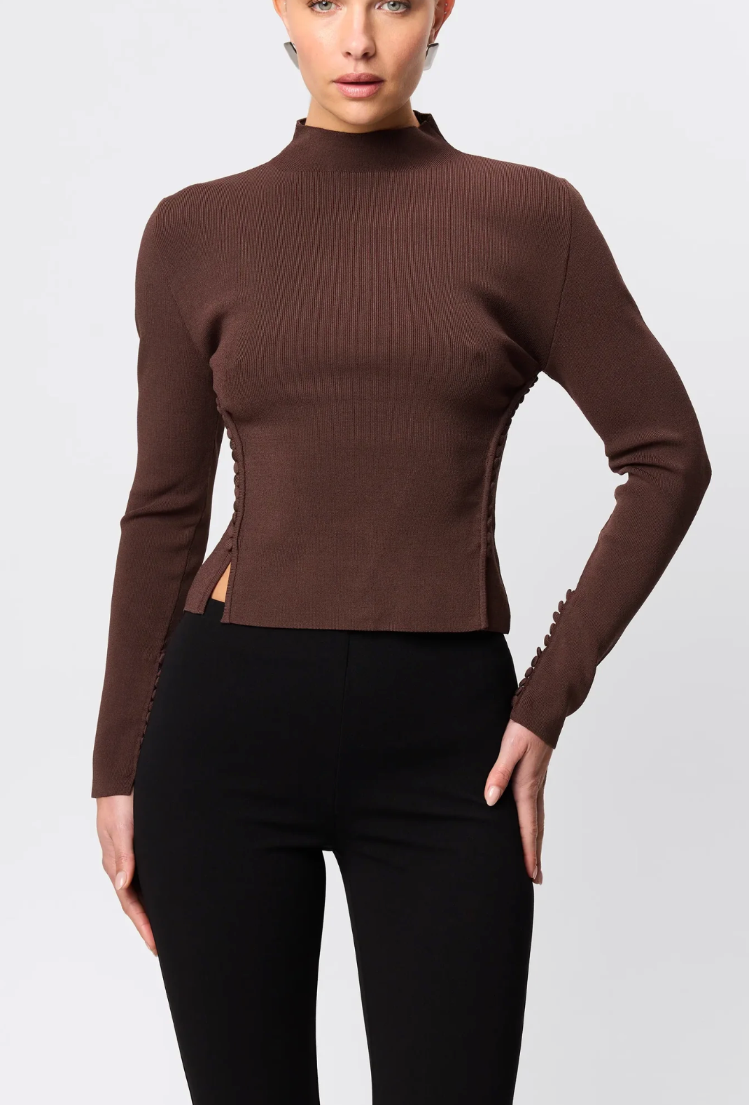 Woman wearing a brown ribbed long-sleeve top and black pants on a white background